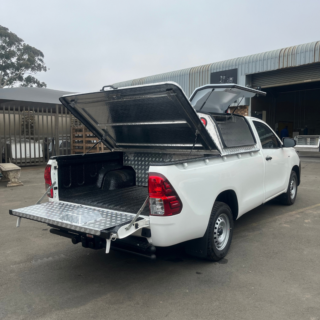 FIELD SERVICE CANOPY WITH A REAR BIN COVER FITTED TO A WHITE ISUZU BAKKIE STANDING IN THE FRONT YARD OF A MANUFATURING WAREHOUSE
